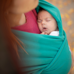 A mother carrying a baby in a green wrap